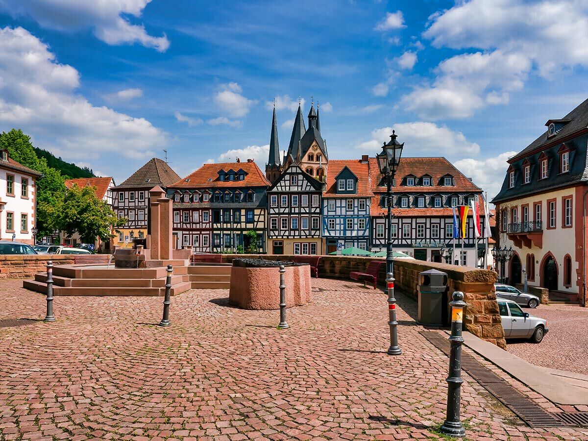 Panorama eines deutschen Marktplatzes mit Fachwerkhäusern, Kirchtürmen und Brunnen unter blauem Himmel.