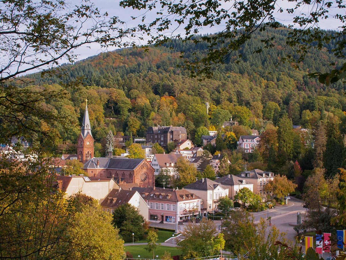 Panoramaansicht einer malerischen Stadt im Schwarzwald mit historischer Kirche, bunten Herbstbäumen und Hügeln.