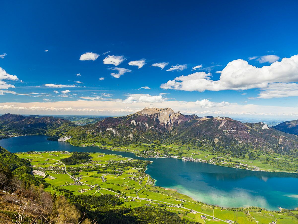 Panoramablick auf Wolfgangsee und Mondsee im Salzkammergut, Österreich, mit grünen Tälern, Dörfern und Bergen unter blauem Himmel.