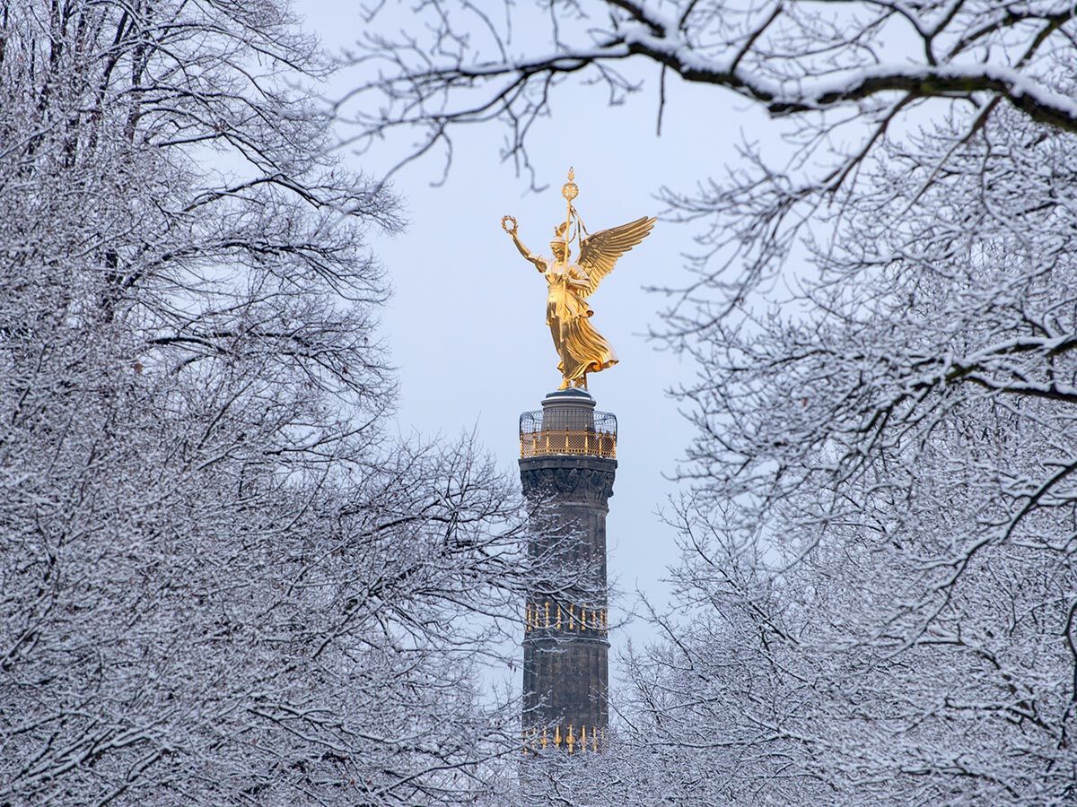 Goldene Viktoria-Statue auf der Berliner Siegessäule, umgeben von schneebedeckten Bäumen an einem Wintertag.