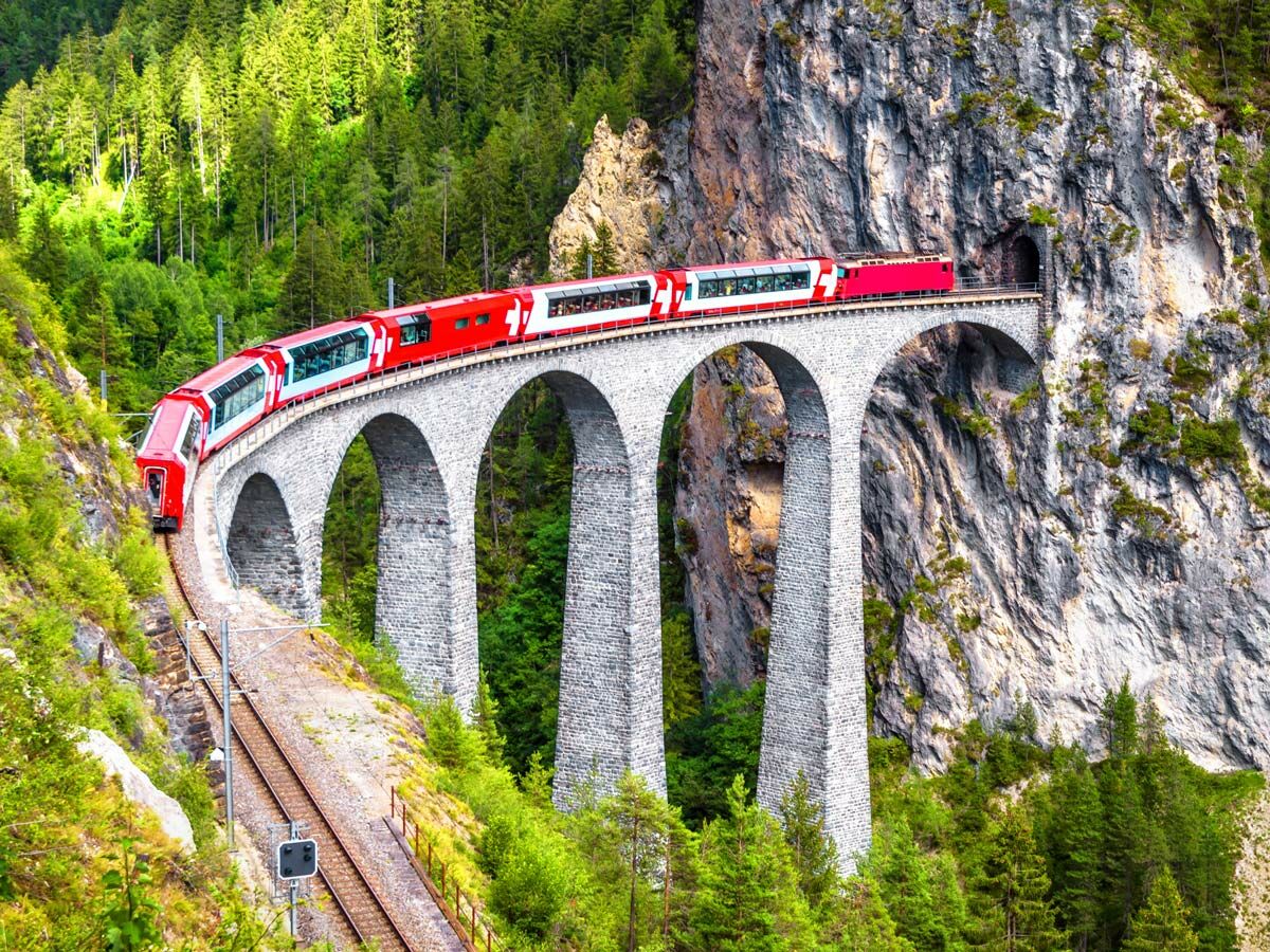 Roter Rhätische Bahn Zug überquert den Landwasser Viadukt in den Schweizer Alpen, umgeben von Wald und Felsen.
