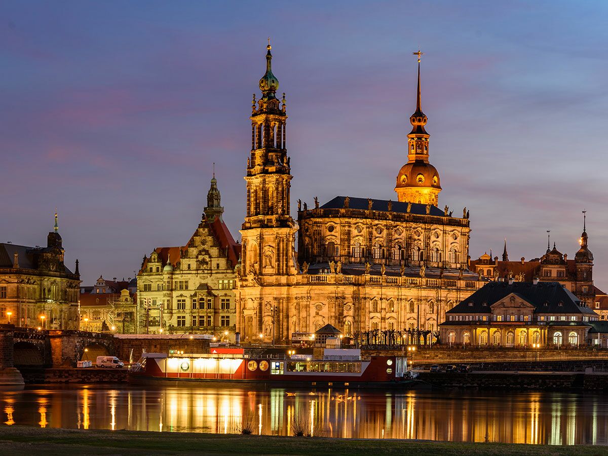 Malerische Nachtansicht von Dresden mit beleuchteten historischen Gebäuden, der Hofkirche, der Elbe und einem Schiff.