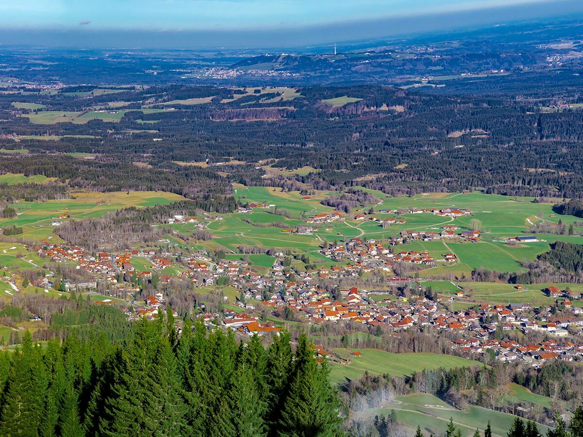 Luftaufnahme eines idyllischen bayerischen Dorfes mit roten Dächern inmitten grüner Wiesen und Wälder im Alpenvorland.