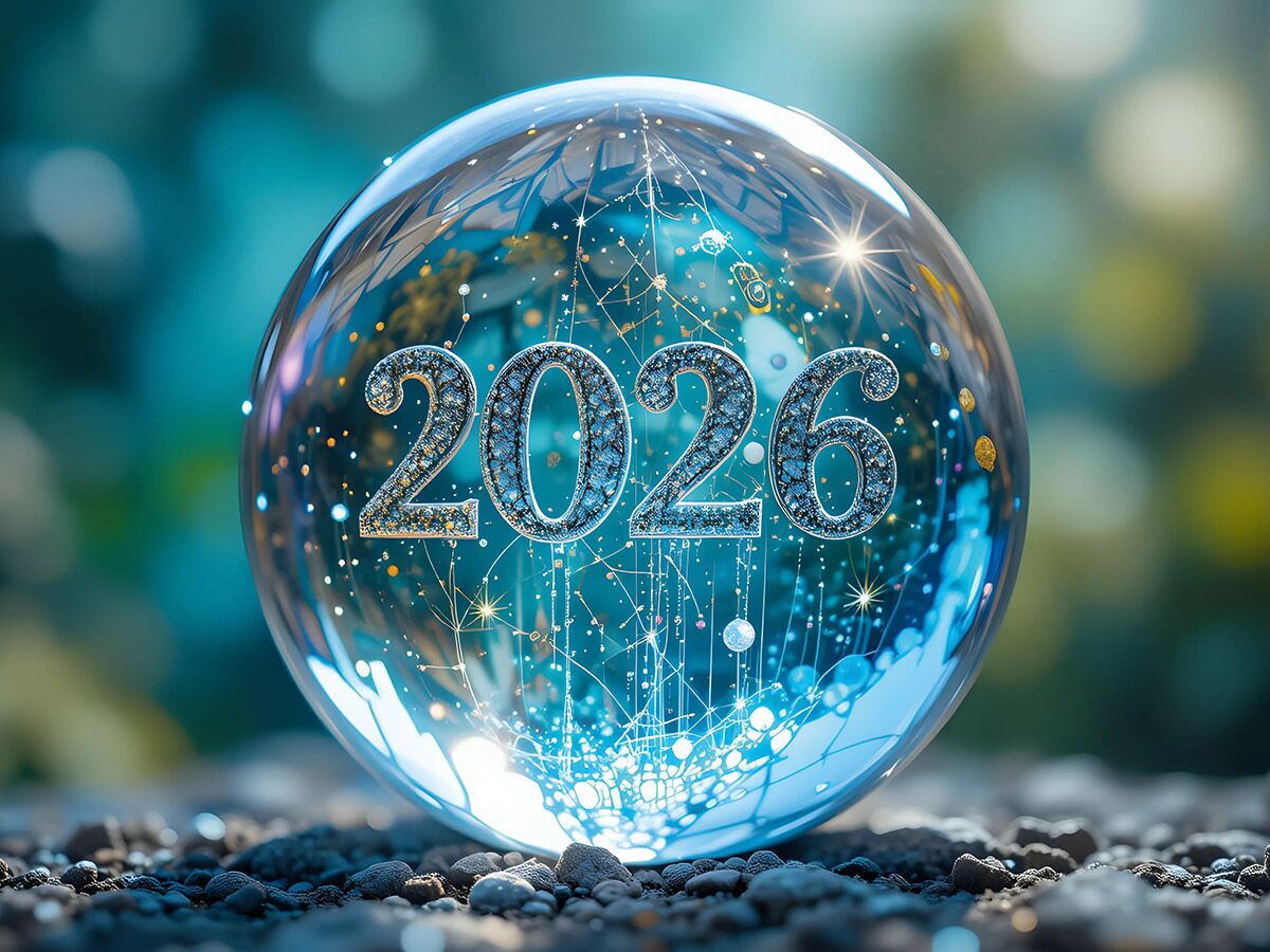 Eine transparente Glaskugel zeigt die Jahreszahl 2026 mit leuchtenden Netzstrukturen auf felsigem Untergrund, umgeben von Bokeh.