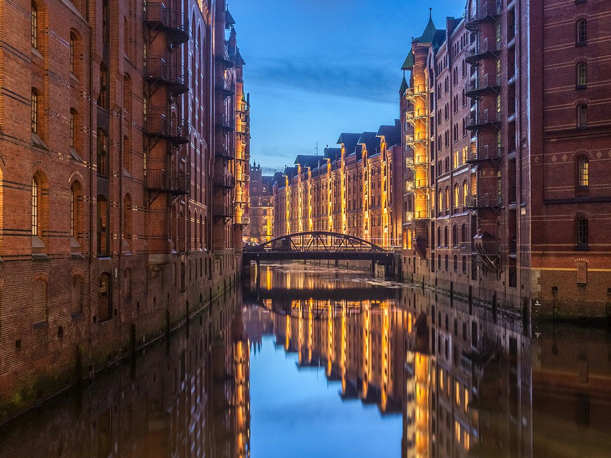 Historische Speicherstadt Hamburg bei Nacht mit beleuchteten Backsteingebäuden, Kanal und Brücke, Spiegelungen im Wasser.