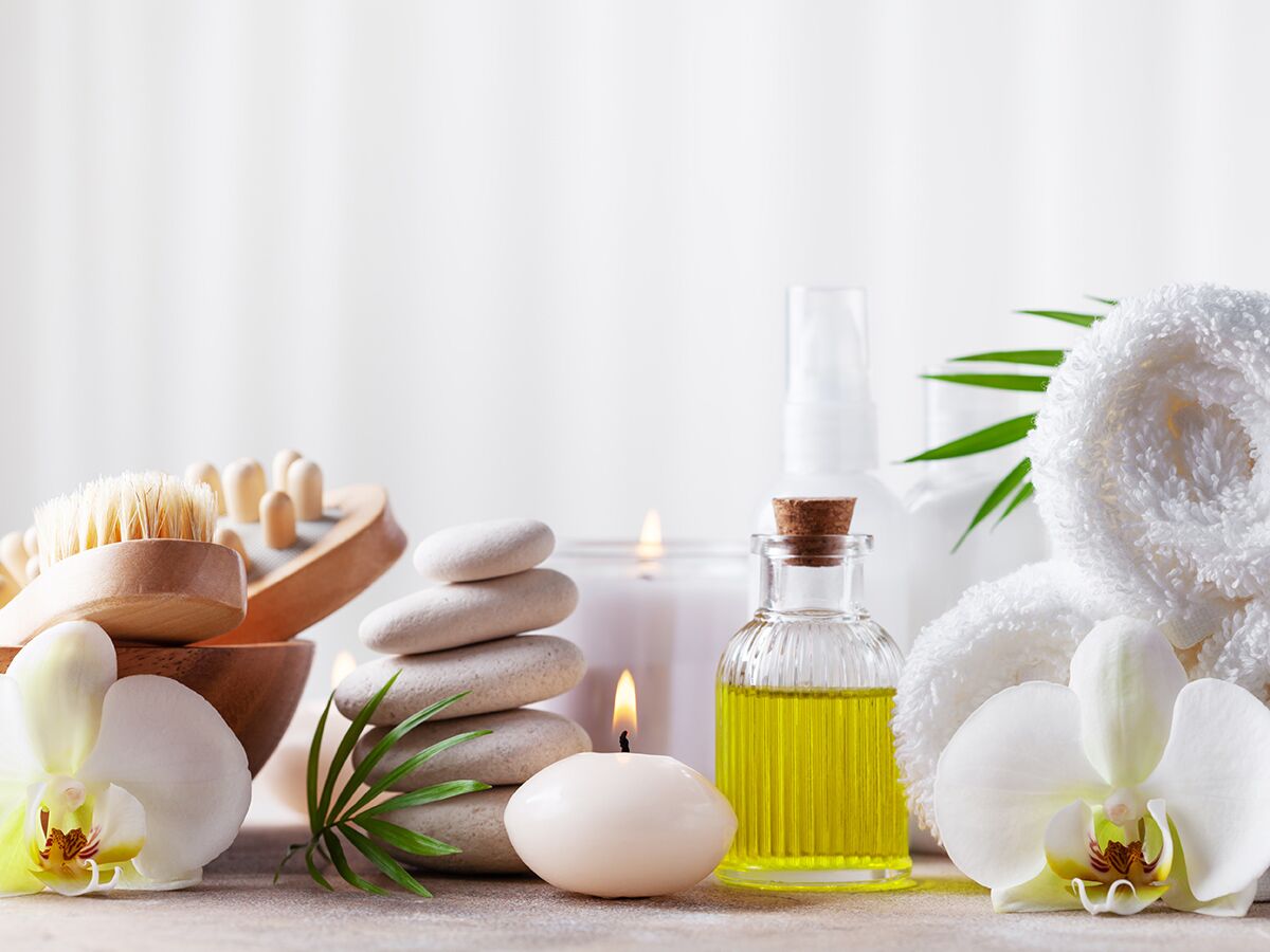 Entspannendes Spa-Set mit weißen Orchideen, Massagewerkzeugen, gestapelten Steinen, brennenden Kerzen und ätherischem Öl.