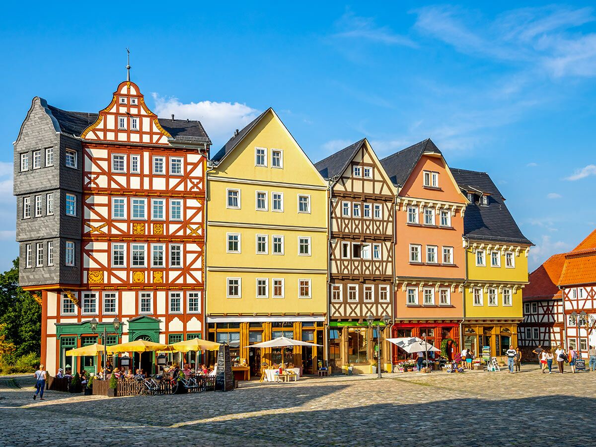 Eine Reihe bunter historischer Fachwerkhäuser an einem sonnigen Marktplatz mit Cafés und Menschen in Deutschland.