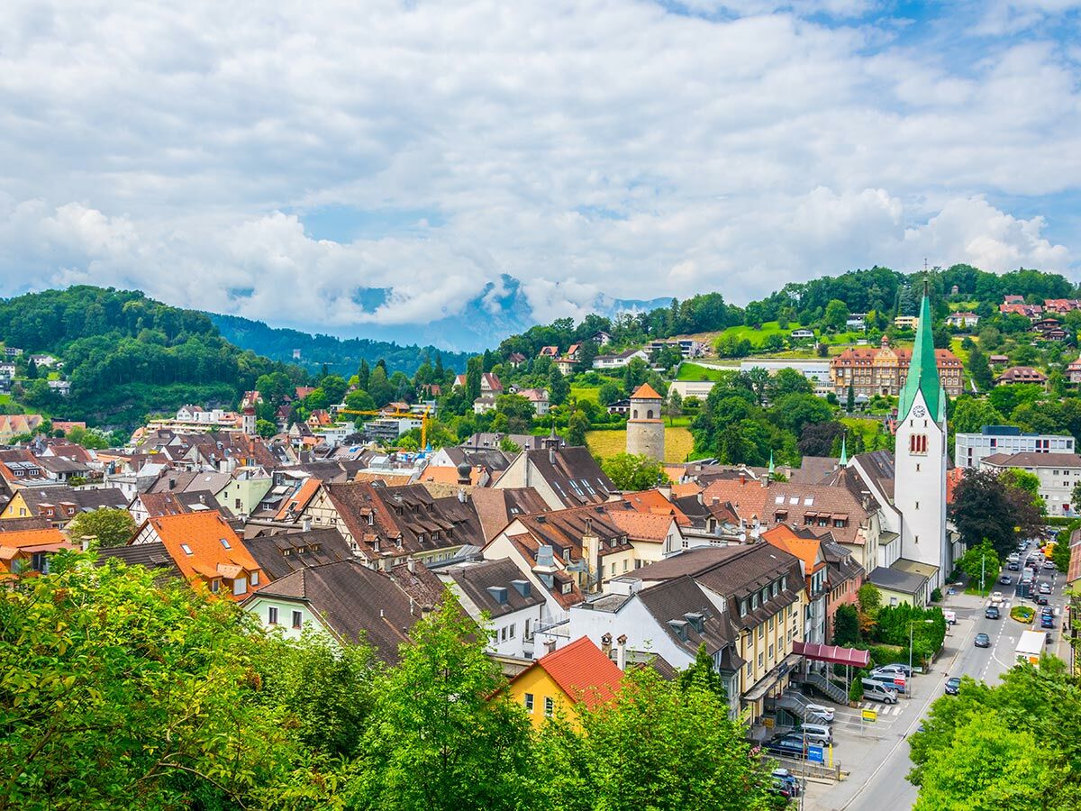 Malerische europäische Stadt im Tal mit vielen Häusern, roten Dächern, einer Kirche mit grünem Turm und grünen Hügeln.