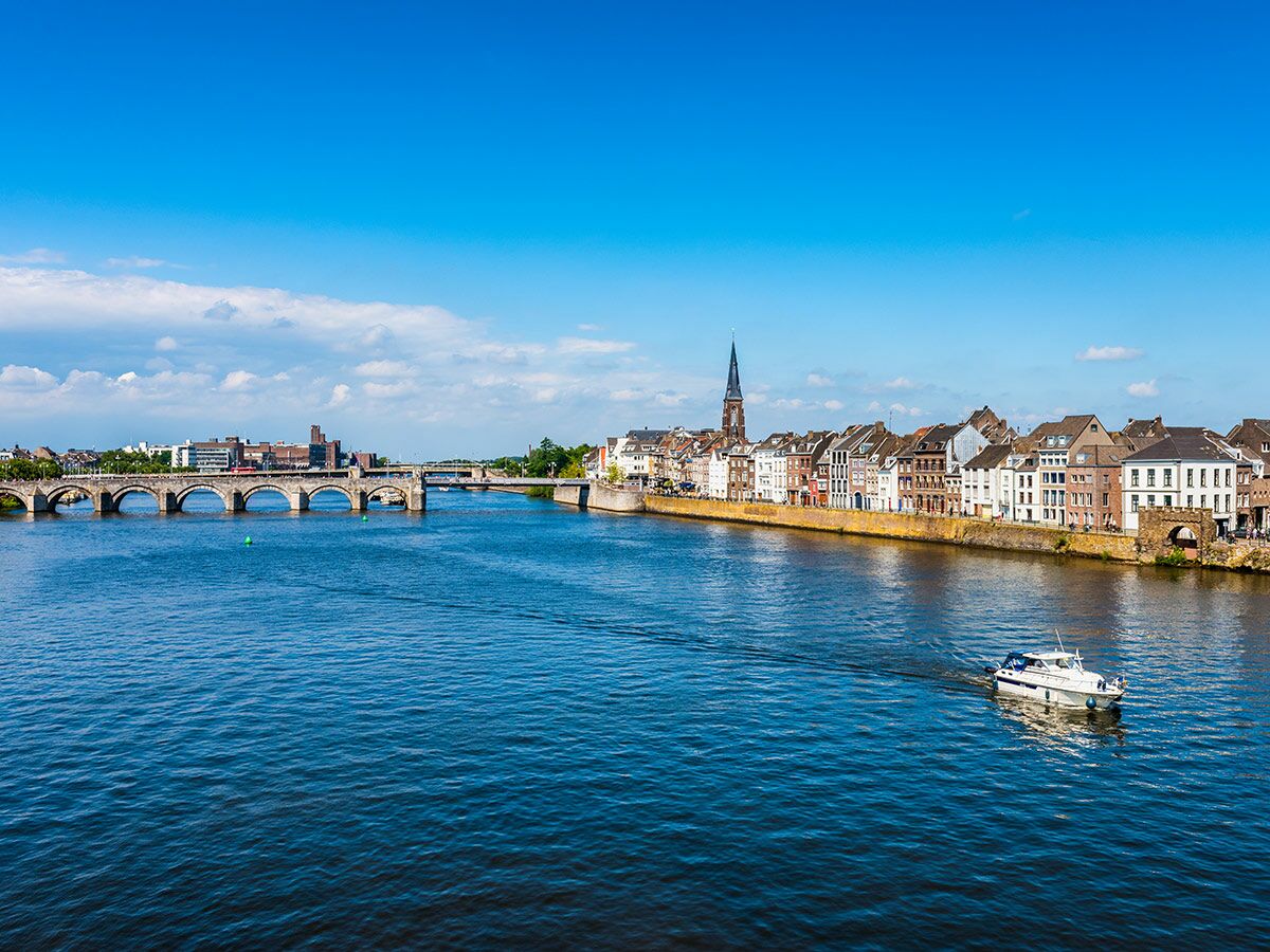 Panoramablick auf Maastricht mit der Sint Servaasbrug über die Maas, historischen Gebäuden am Ufer und Boot.