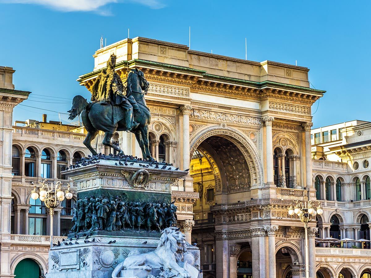 Reiterstatue von König Victor Emanuel II. vor der prächtigen Galleria Vittorio Emanuele II. in Mailand bei blauem Himmel.