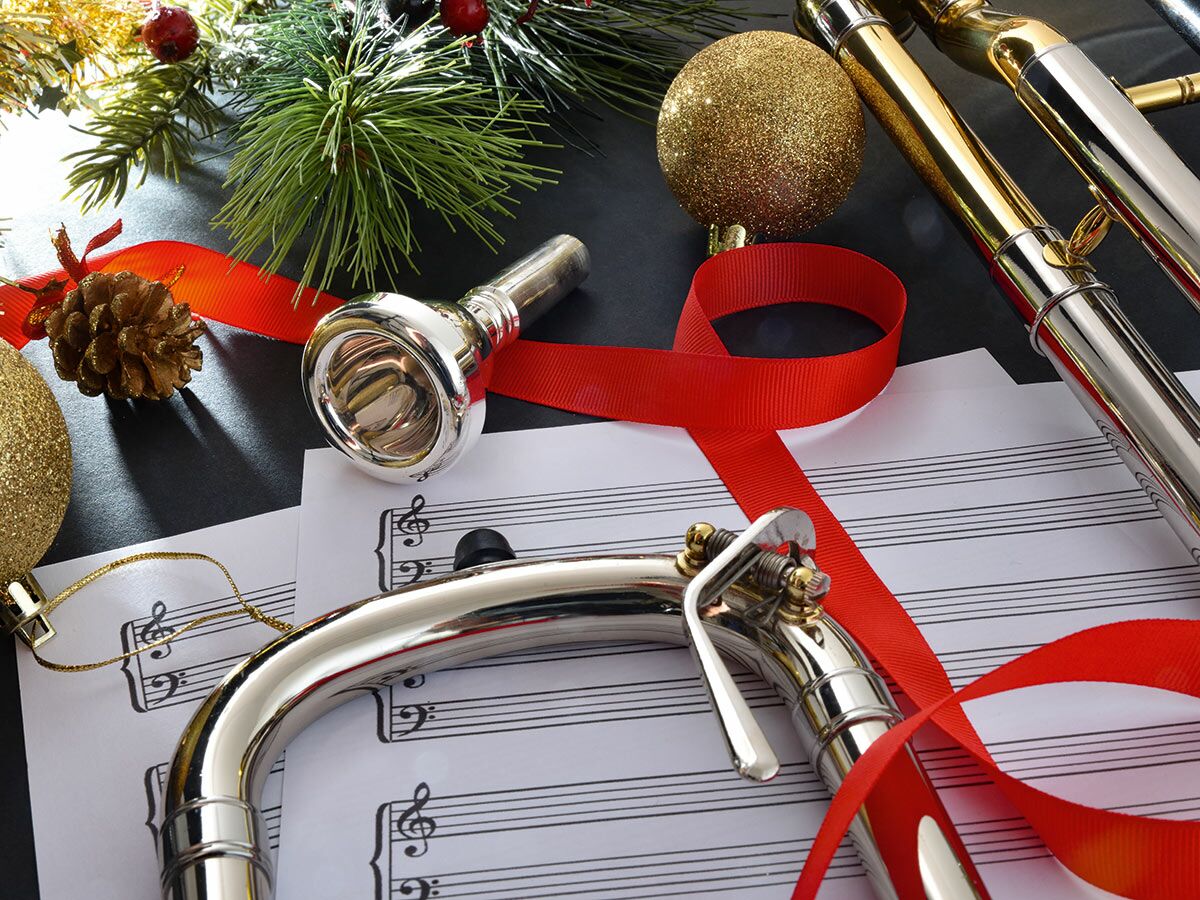 Festliche Posaune mit Mundstück, Notenblättern, roten Bändern, goldenen Kugeln und Tannenzweigen für Weihnachtsmusik.