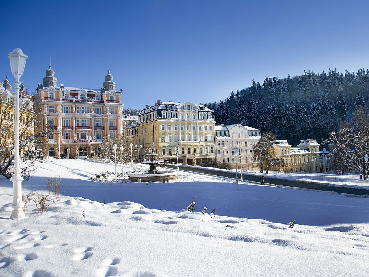 Panoramablick auf die verschneite Winterlandschaft von Mariánské Lázně mit dem Grandhotel Esplanade unter blauem Himmel.