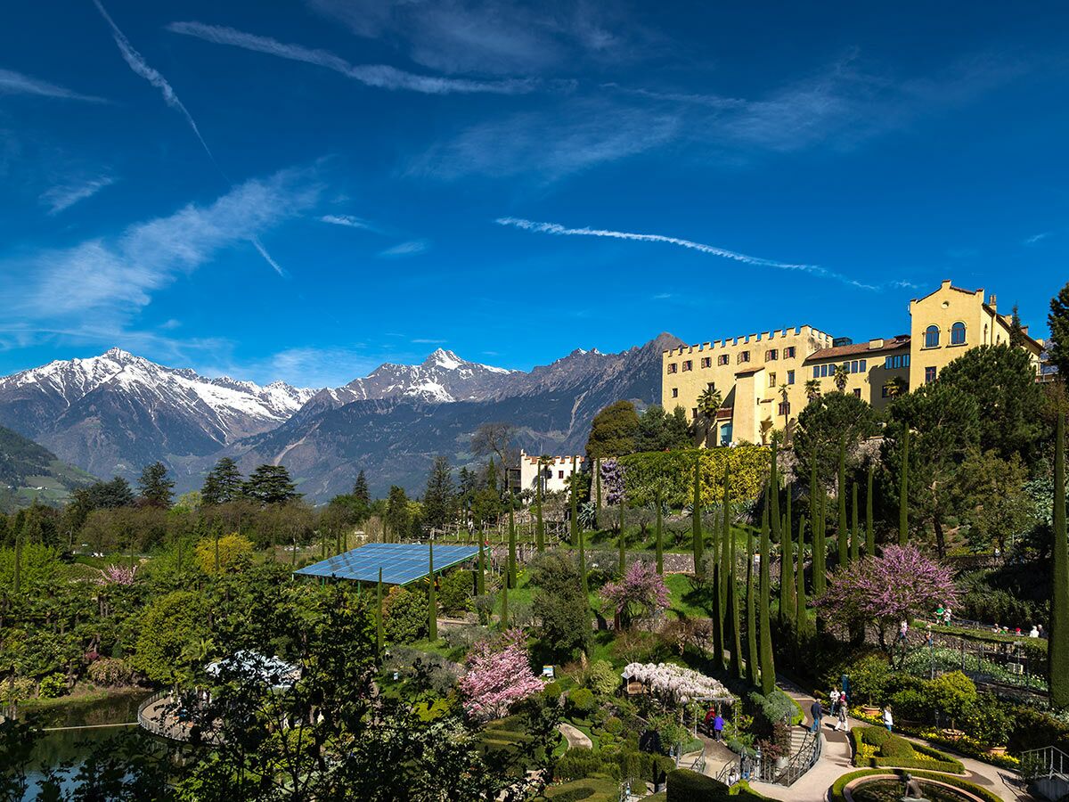 Schloss Trauttmansdorff und Botanische Gärten in Meran, Südtirol, mit blühenden Bäumen, Teich, Solaranlage und Alpenpanorama.