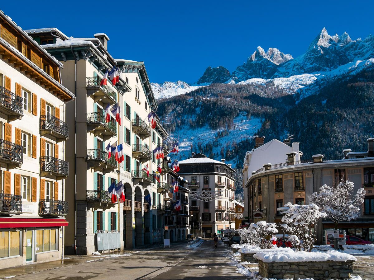Malerische Chamonix Dorfstraße mit französischen Flaggen, verschneiten Gebäuden und majestätischen Mont Blanc Bergen.