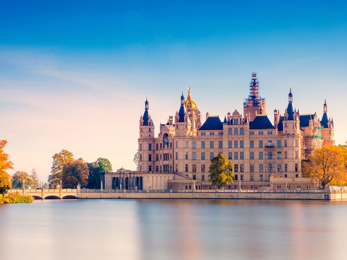 Majestätisches Schweriner Schloss am See, umgeben von Herbstbäumen mit goldener Morgenbeleuchtung.