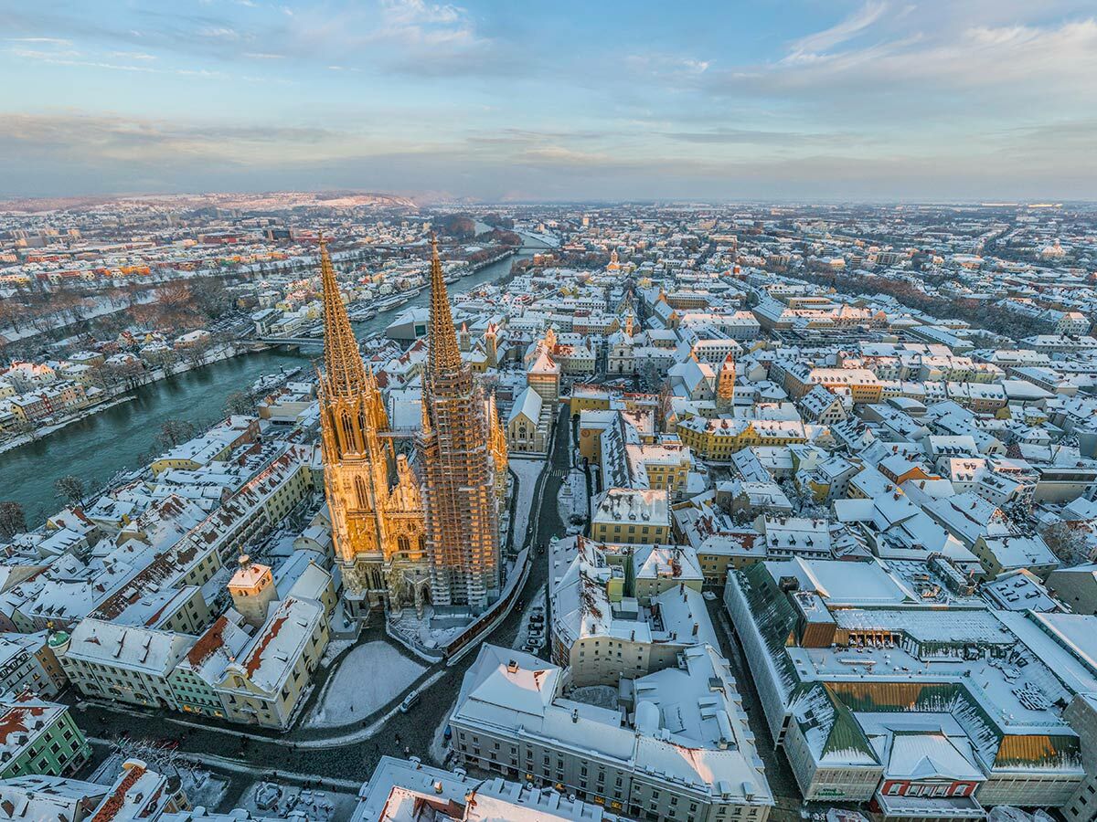 Luftbild von Regensburg im Winter: Der Dom St. Peter und verschneite Dächer an der Donau im goldenen Licht.