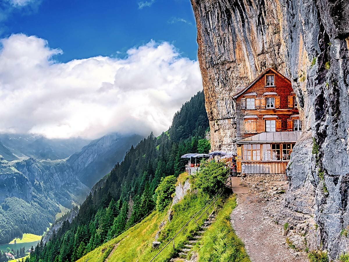 Spektakuläres Berggasthaus Aescher in einer Felswand eingebettet, umgeben von Alpenpanorama, Wald und See.