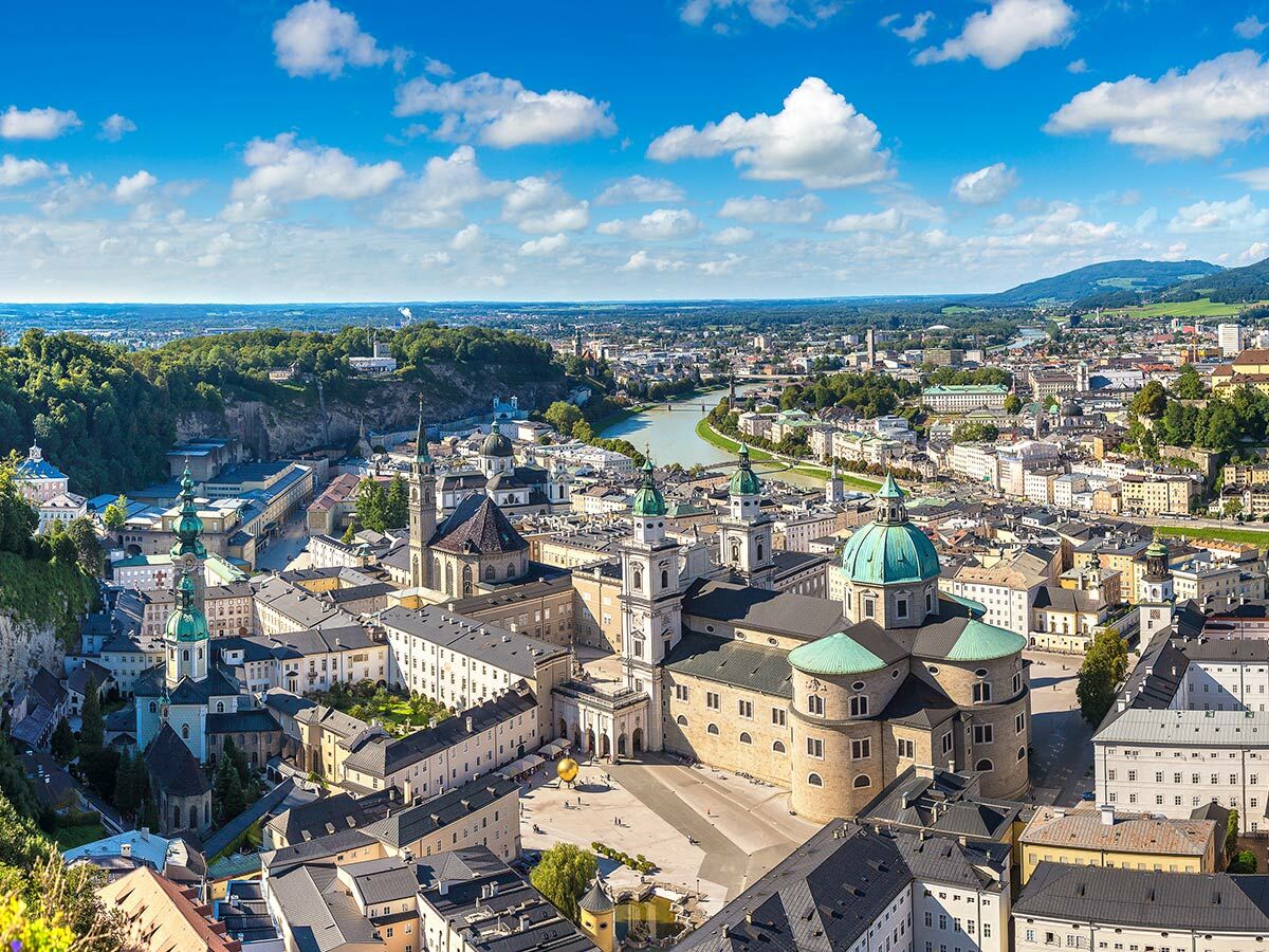 Luftbild von Salzburg mit Kathedrale, Salzach Fluss, historischen Gebäuden und Bergen unter blauem Himmel.