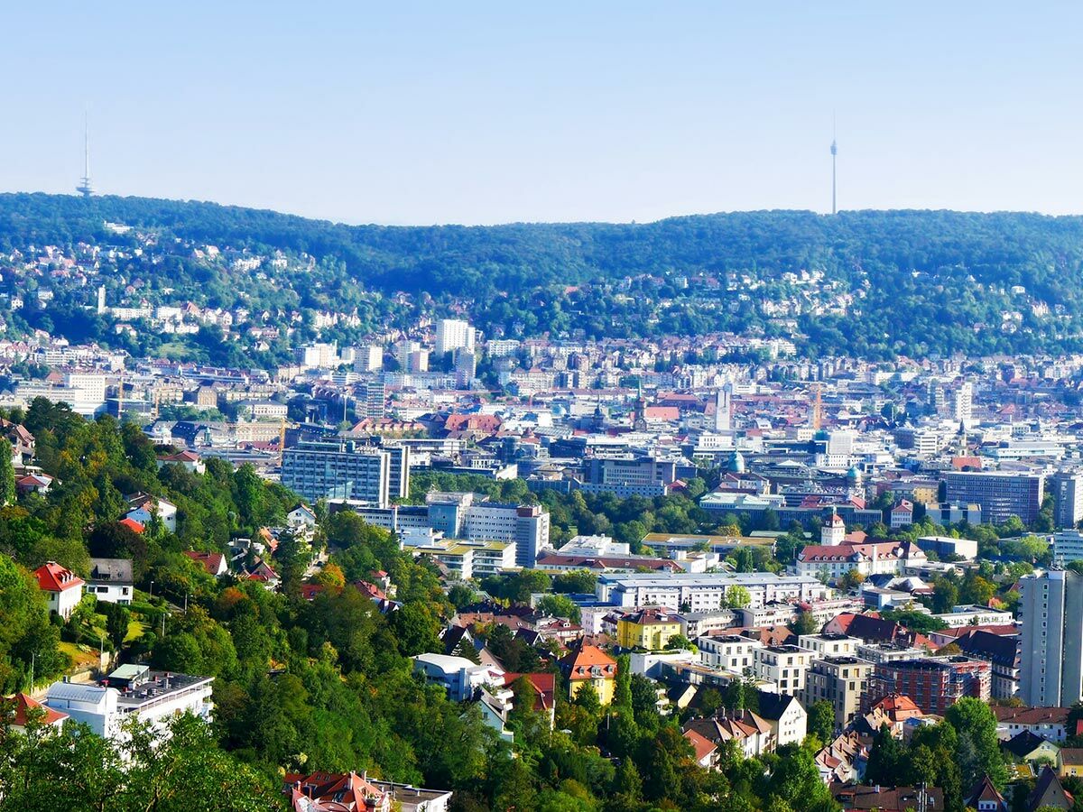 Panoramablick auf Stuttgart mit grünen Hügeln, dem Fernsehturm und Stadtgebäuden bei Sonnenschein.