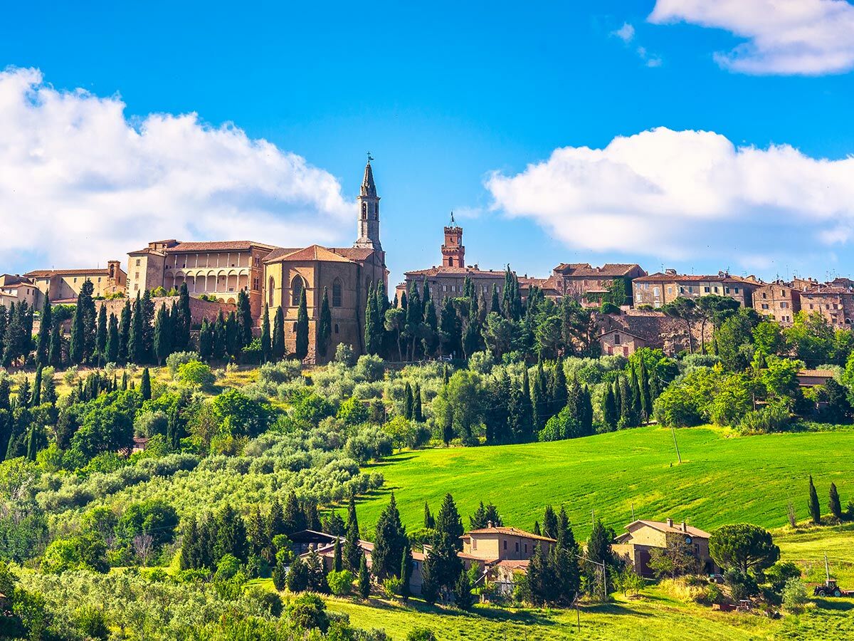 Panoramablick auf eine historische Hügelstadt in der Toskana, Italien, mit Zypressen, Olivenhainen und grünen Feldern.