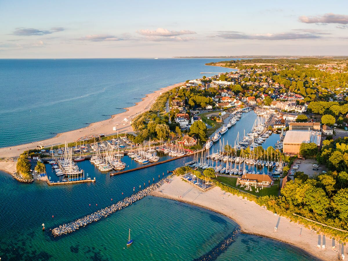 Luftbild von Kühlungsborn Hafen mit zahlreichen Segelbooten, langem Sandstrand und Küstenstadt an der Ostsee bei Sonnenuntergang.