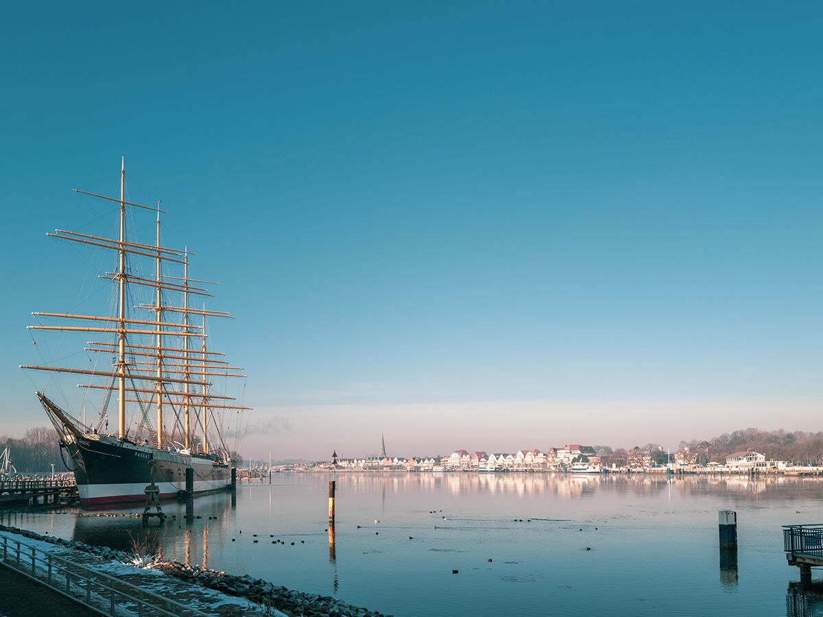 Das historische Segelschiff Passat liegt im winterlichen Hafen von Travemünde, mit ruhigem Wasser und einer Stadtkulisse im Hintergrund.