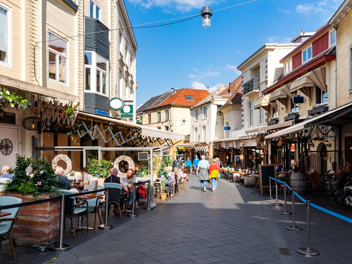 Lebhafte europäische Fußgängerzone mit Straßencafés, historischen Gebäuden und Menschen an einem sonnigen Tag.