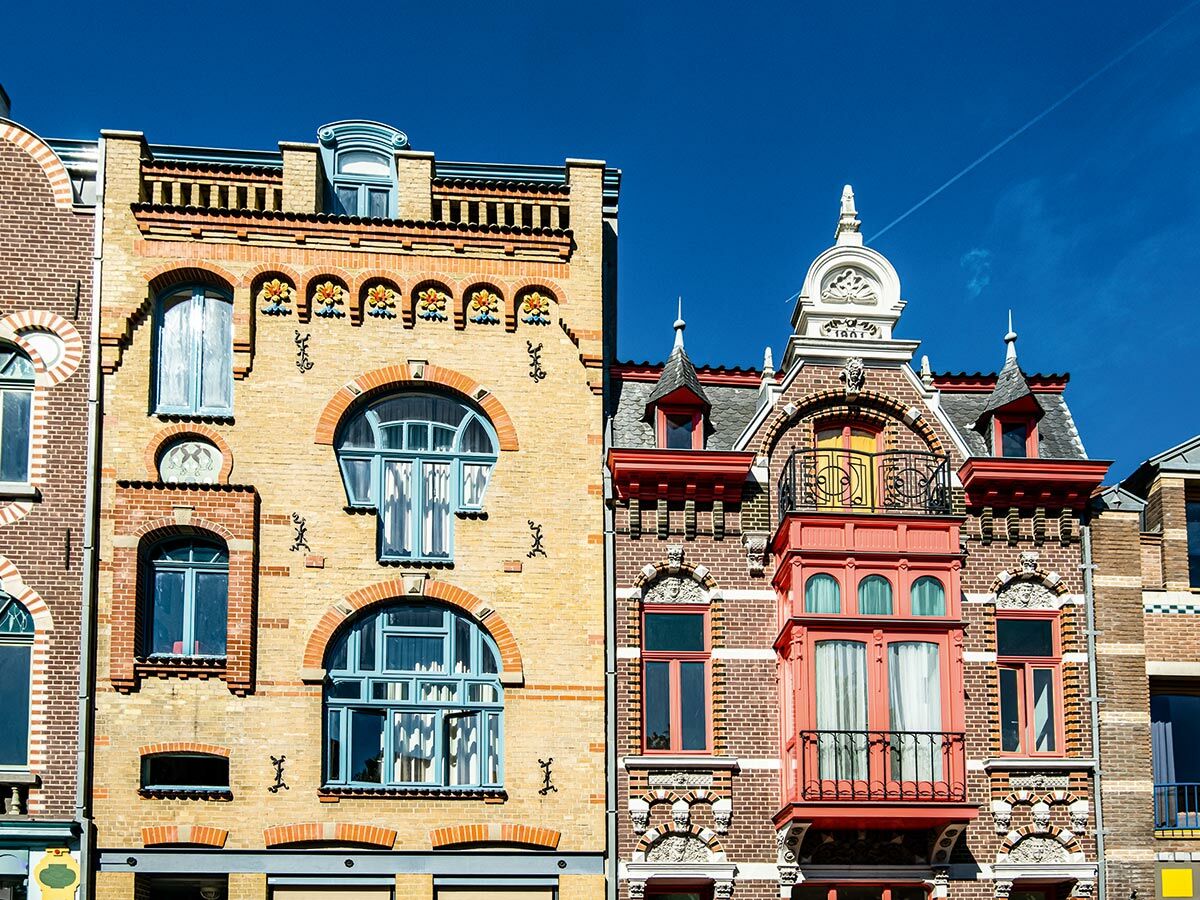 Zwei farbenfrohe historische Gebäude mit kunstvollen Fassaden, blauen Fenstern und roten Akzenten unter strahlend blauem Himmel.