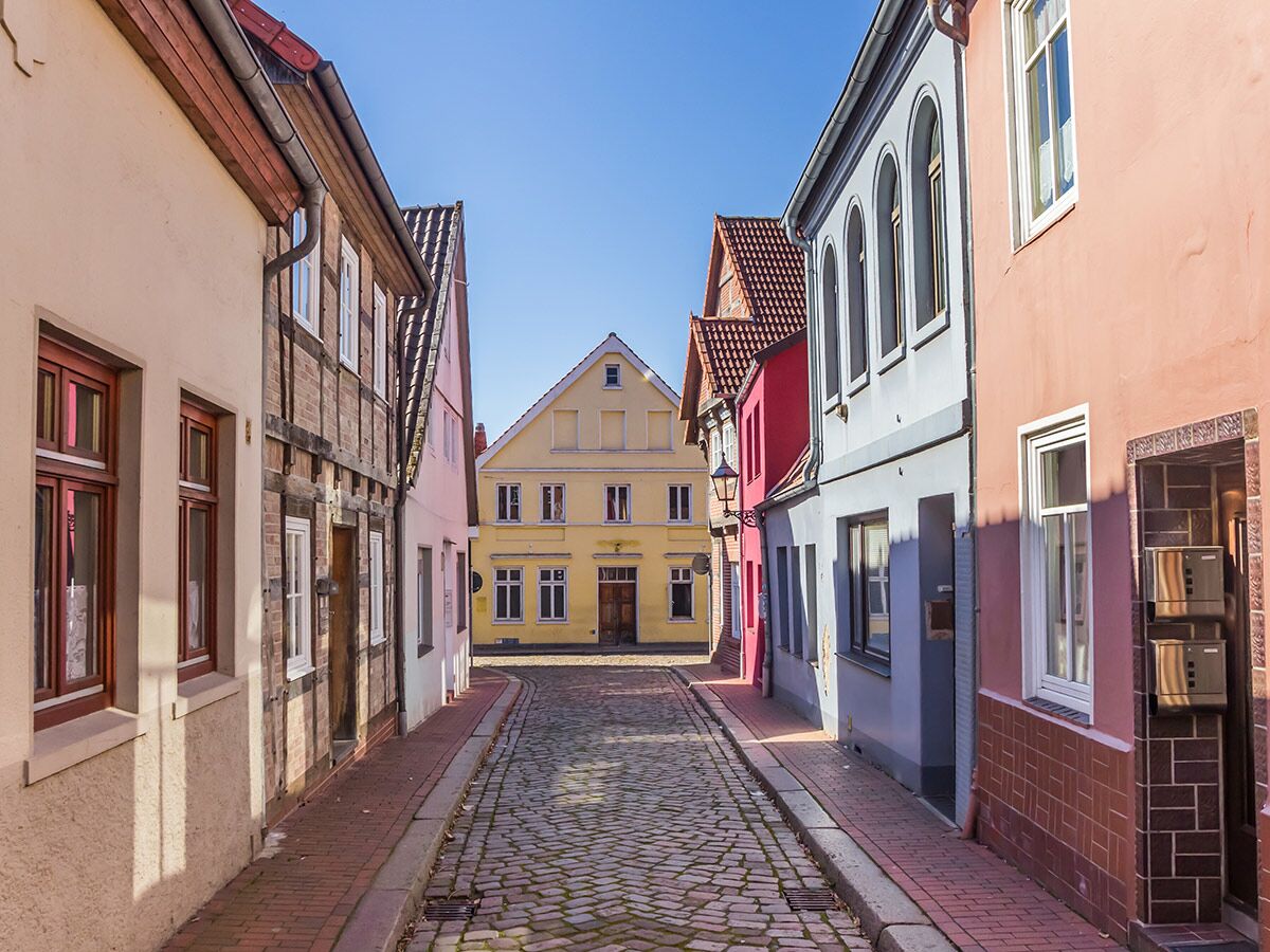 Blick durch eine sonnige, kopfsteingepflasterte Altstadtgasse mit vielen bunten, historischen Häusern und Fachwerkhäusern.