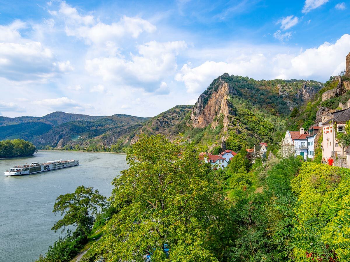 Panoramablick auf die Wachau mit einem Kreuzfahrtschiff auf der Donau, umgeben von grünen Hügeln und einem historischen Dorf.