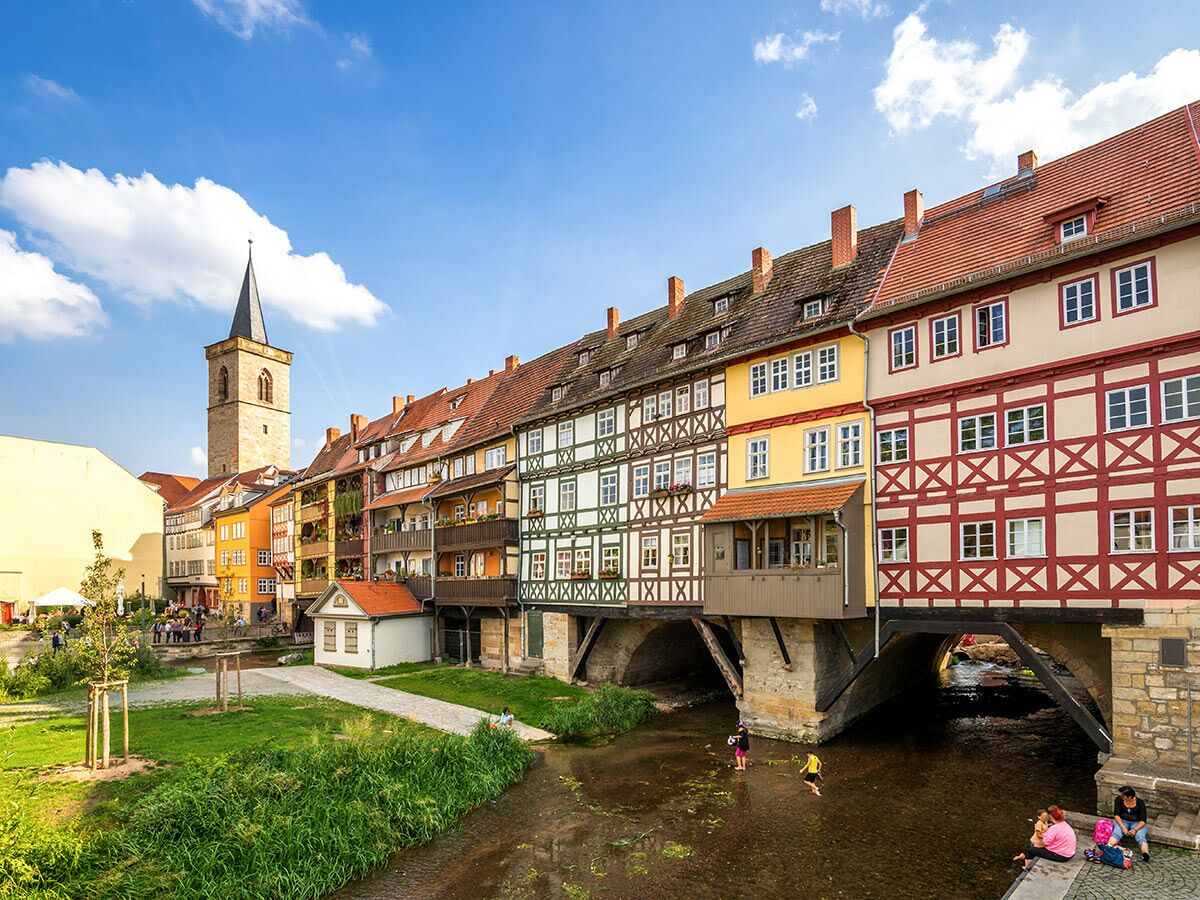 Die Krämerbrücke in Erfurt mit bunten Fachwerkhäusern über dem Fluss Gera, unter blauem Himmel und Wolken.