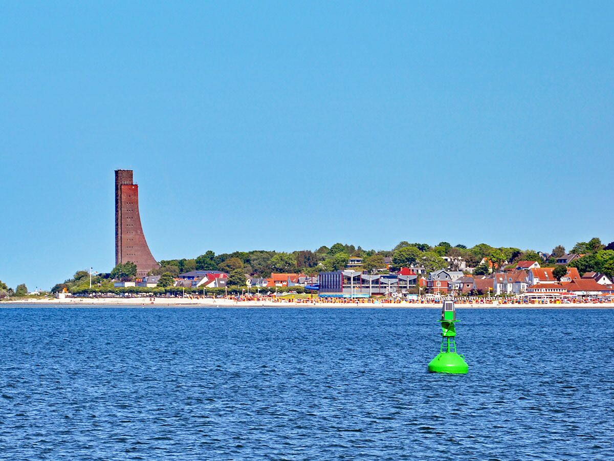 Panoramablick auf das Marine-Ehrenmal Laboe, belebten Strand, blaue Ostsee und grüne Boje bei Sonnenschein.