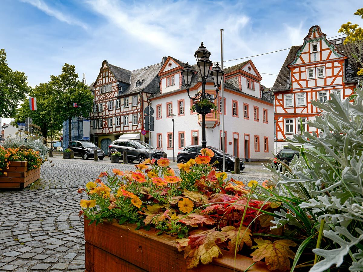 Idyllische Altstadtgasse in Deutschland mit historischen Fachwerkhäusern, Kopfsteinpflaster, Blumenkästen und geparkten Autos.