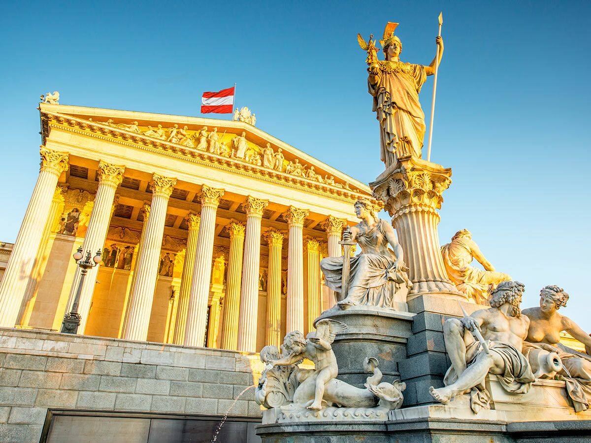 Österreichisches Parlament und Pallas-Athena-Brunnen in Wien bei Sonnenuntergang mit blauer Himmel.