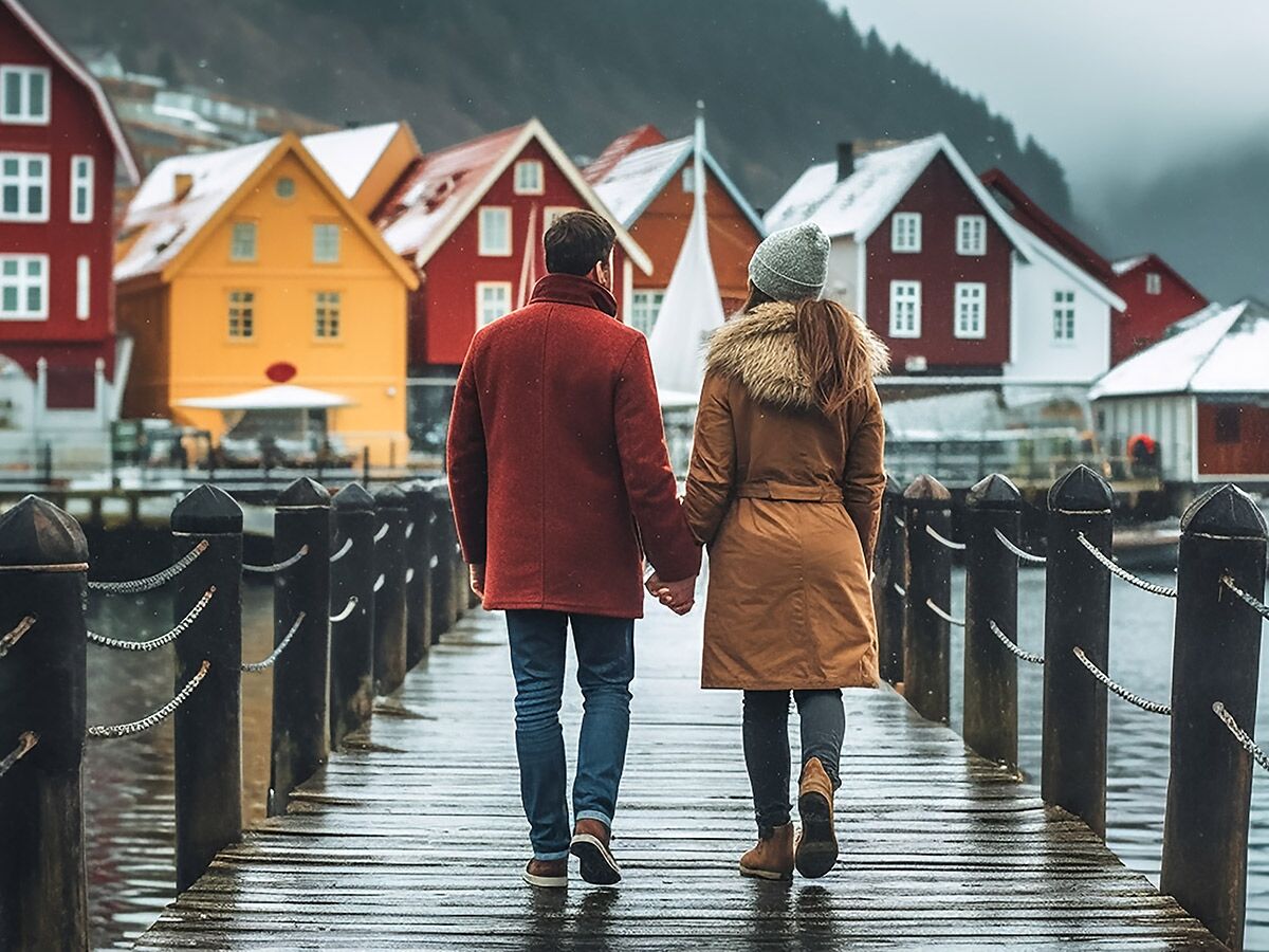 Romantischer Spaziergang eines Paares Hand in Hand auf einem Holzsteg in einem bunten Fischerdorf mit Schnee.