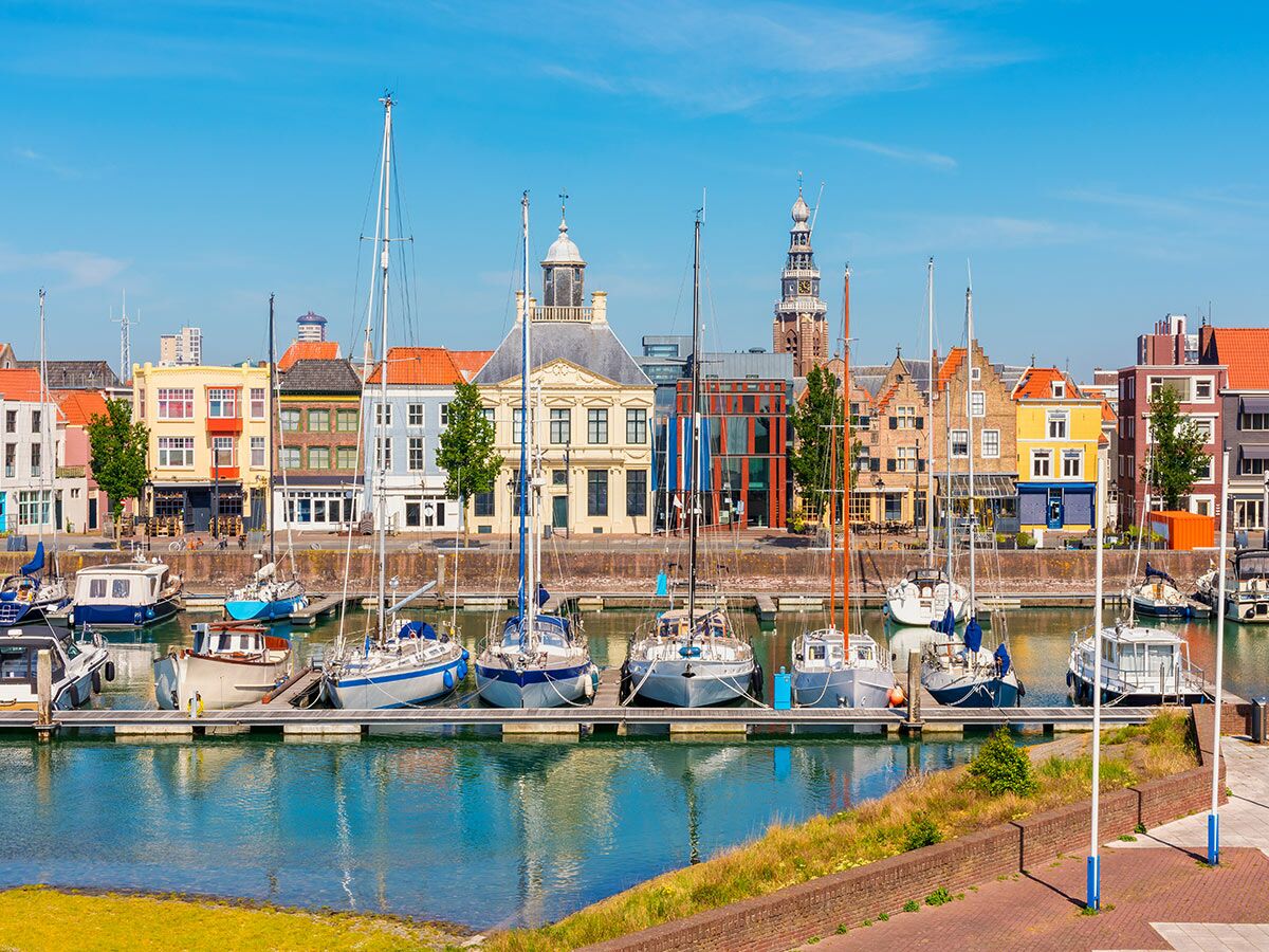 Blick auf den historischen Hafen von Enkhuizen, Niederlande, mit Segelbooten, bunten Gebäuden und dem Drommedaris unter blauem Himmel.