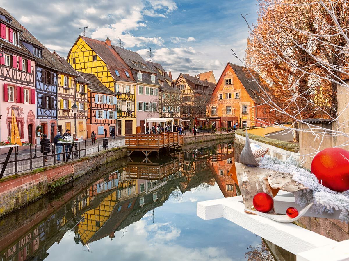 Malerische Fachwerkhäuser am Kanal in Colmar, Frankreich, mit Weihnachtsdekoration und Menschen im Winter.
