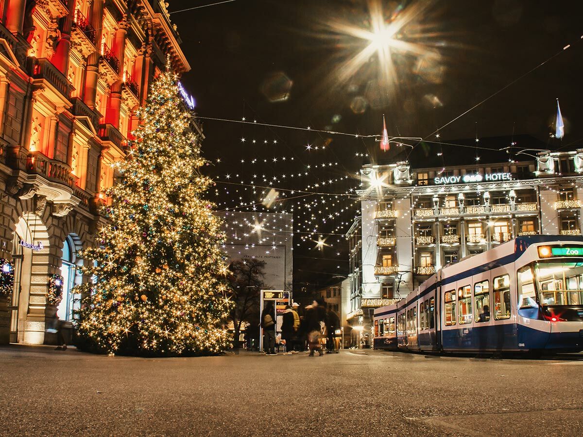 Festlich beleuchteter Weihnachtsbaum und Tram vor dem Savoy Baur en Ville Hotel in Zürich bei Nacht.