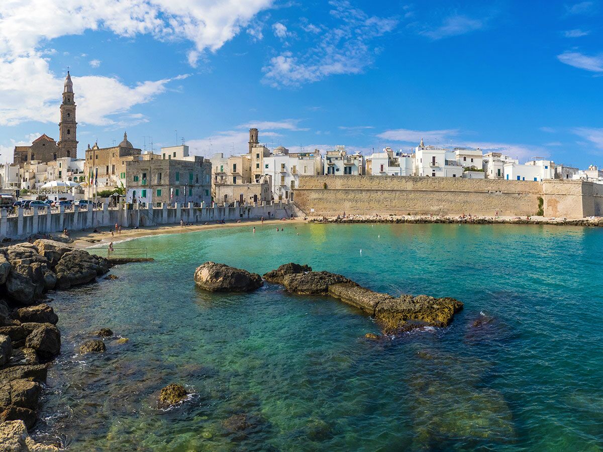 Malerische Küstenstadt Monopoli, Apulien, Italien, mit Strand, türkisem Meer und historischer Architektur unter blauem Himmel.