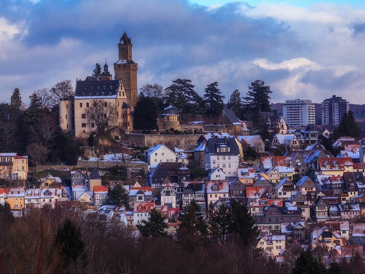 Panoramablick auf historische Burg und verschneite Stadt mit traditionellen Häusern im Winter unter bewölktem Himmel.