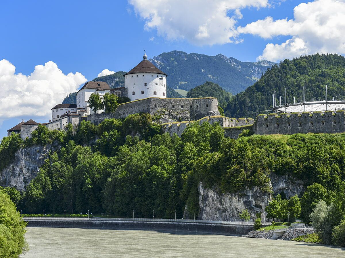 Historische Festung Kufstein in Österreich auf Felsen über dem Fluss Inn, umgeben von grünen Wäldern und Bergen.