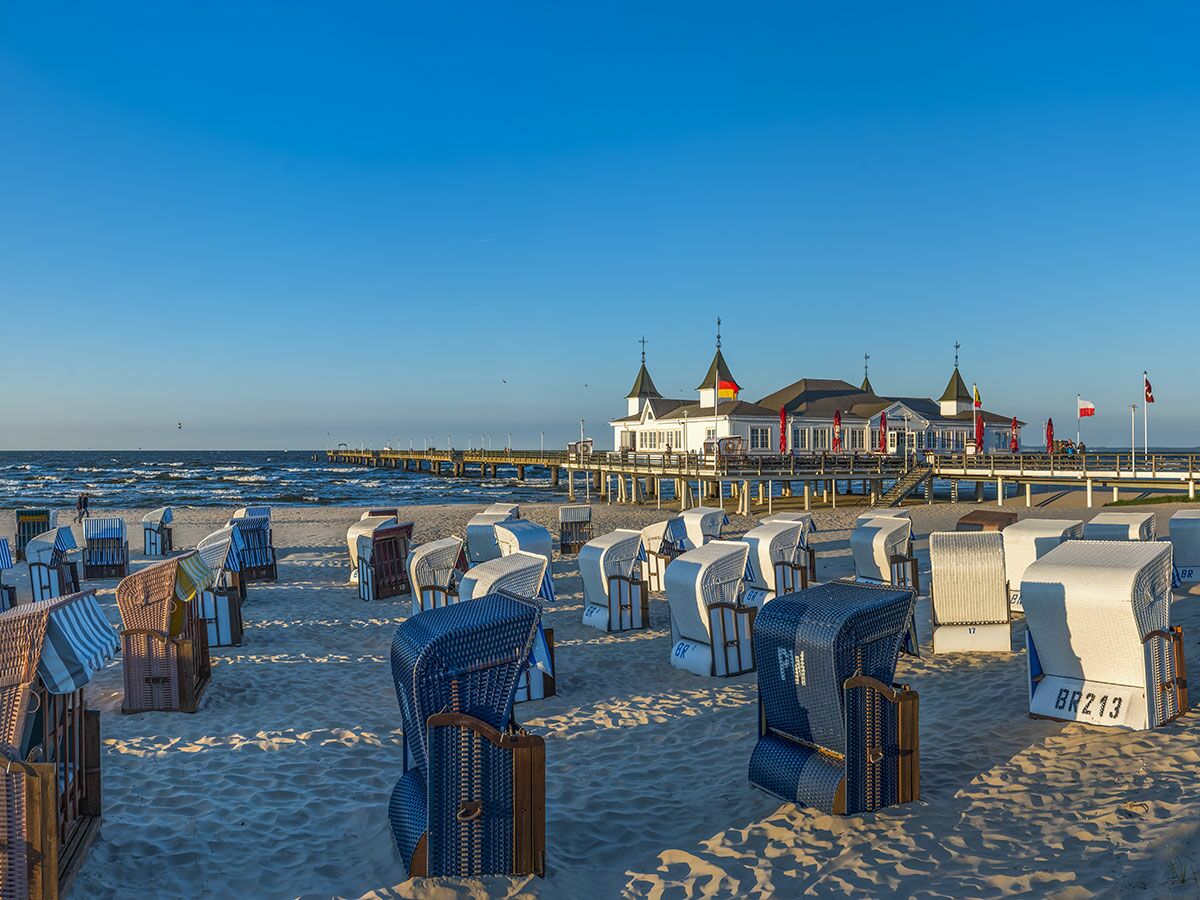 Malerische Seebrücke über dem Meer, mit zahlreichen Strandkörben am sandigen Strand und Abendsonne. Idyllische Küstenlandschaft.