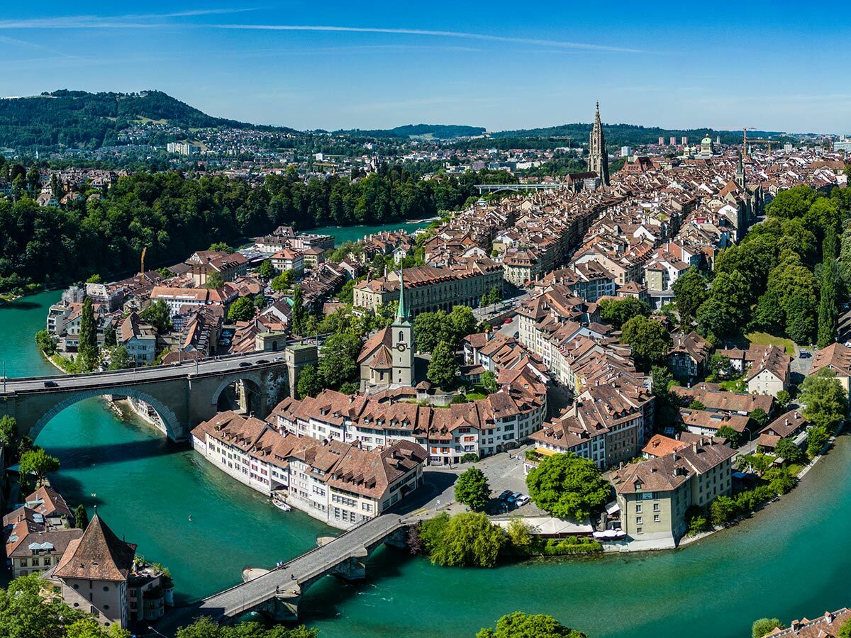 Luftaufnahme der Berner Altstadt in der Schweiz mit der Aare, historischen Gebäuden, Kathedrale und Brücken bei Sonnenschein.