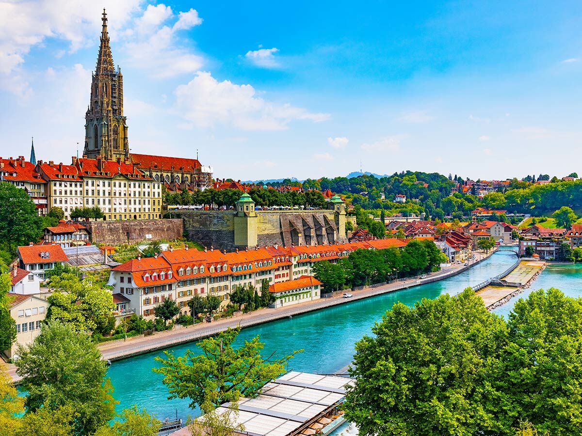 Panoramablick auf die historische Altstadt von Bern, Schweiz, mit dem Berner Münster, der Aare und roten Dächern unter blauem Himmel.