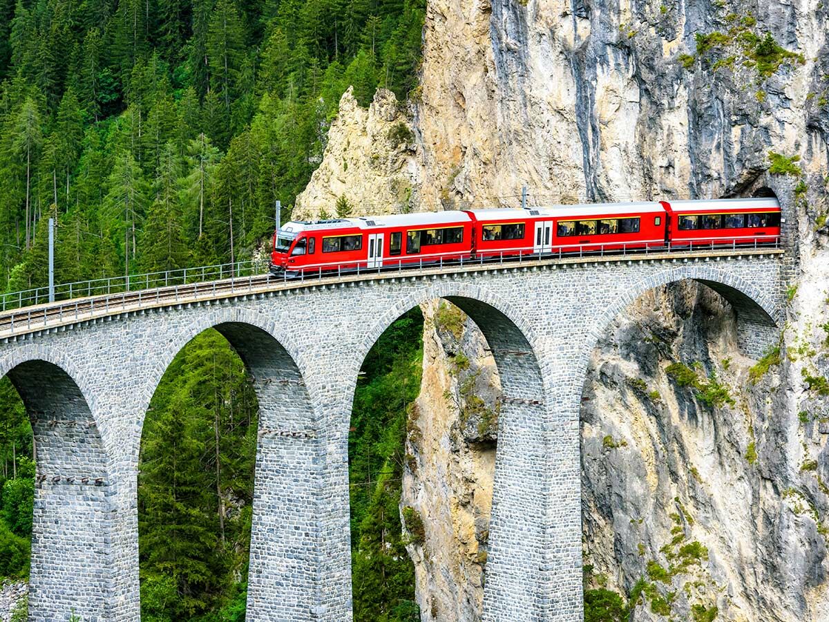Roter Zug der Rhätischen Bahn fährt über den Landwasserviadukt durch grüne Wälder und Felsen in der Schweiz.