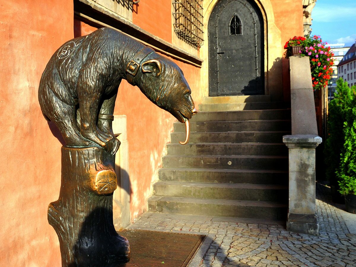 Bronze-Bär-Statue mit Zunge vor historischem Gebäude, Treppe und Bogen-Tür in Wrocław, Polen.