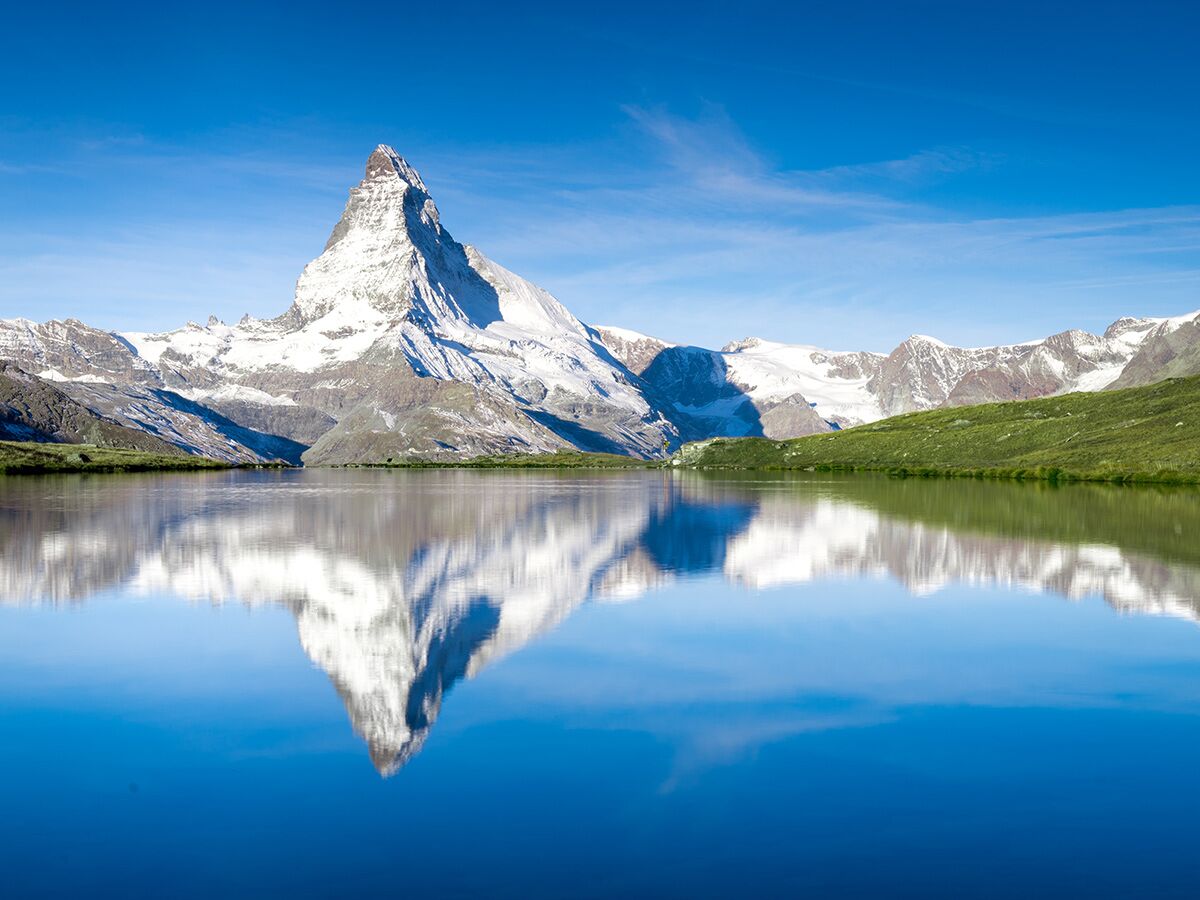 Majestätisches Matterhorn mit schneebedeckter Spitze spiegelt sich perfekt im ruhigen Bergsee unter blauem Himmel wider.