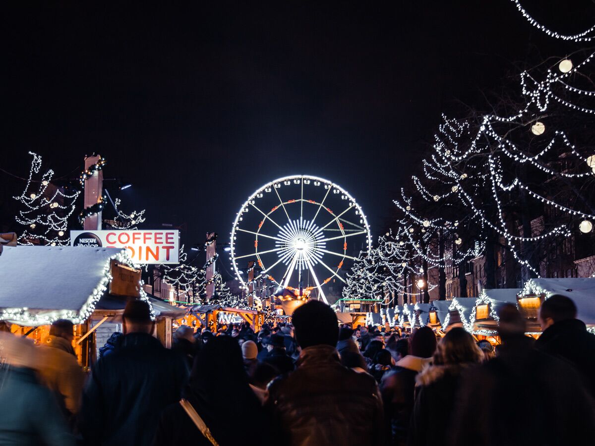 Beleuchteter Weihnachtsmarkt bei Nacht mit Riesenrad, geschmückten Bäumen und vielen Menschen.