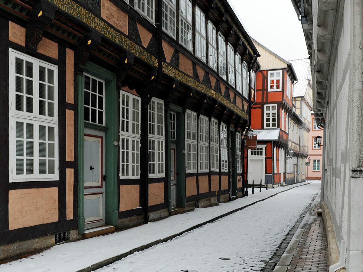 Verschneite Gasse mit bunten Fachwerkhäusern in einer historischen Altstadt im Winter.