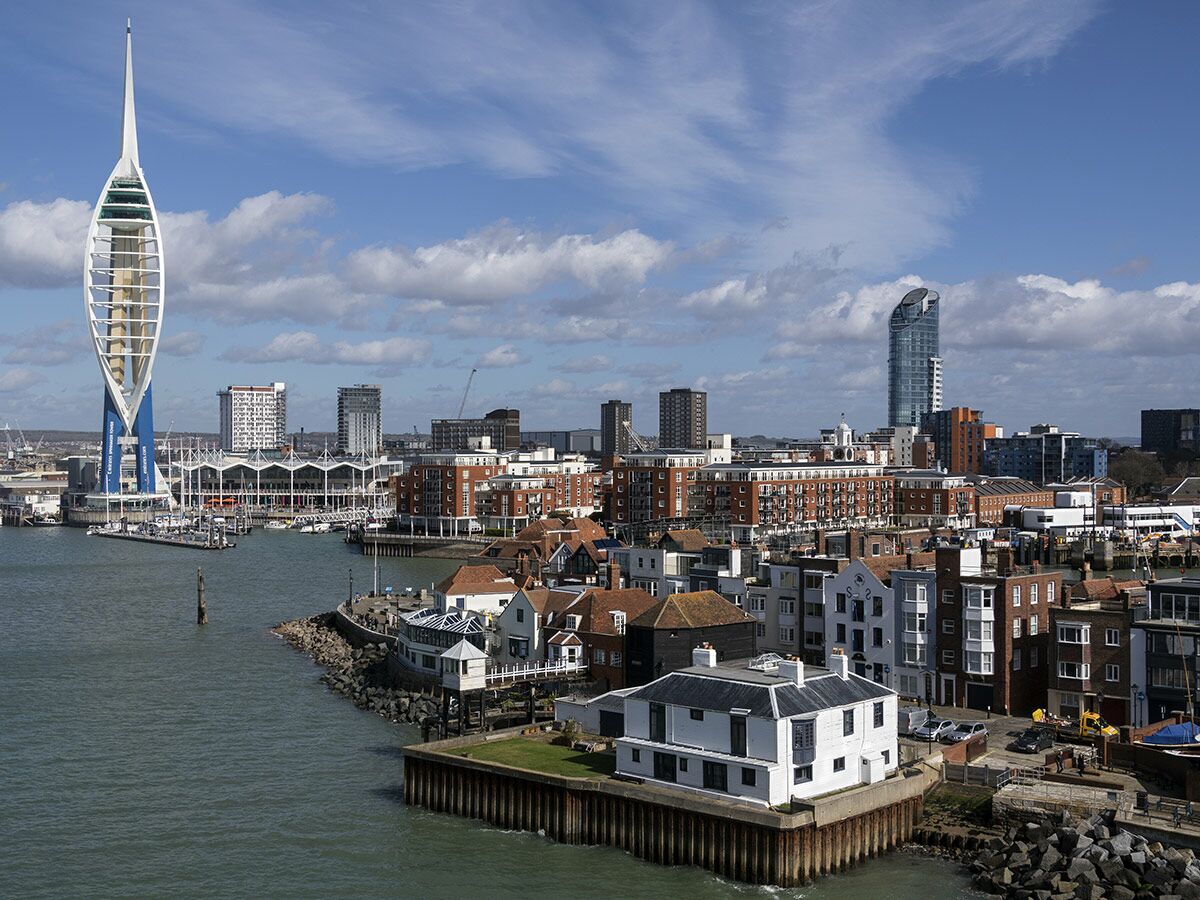 Panoramablick auf Portsmouth mit dem markanten Spinnaker Tower, dem belebten Hafen und einer Mischung aus historischen und modernen Gebäuden unter blauem Himmel.